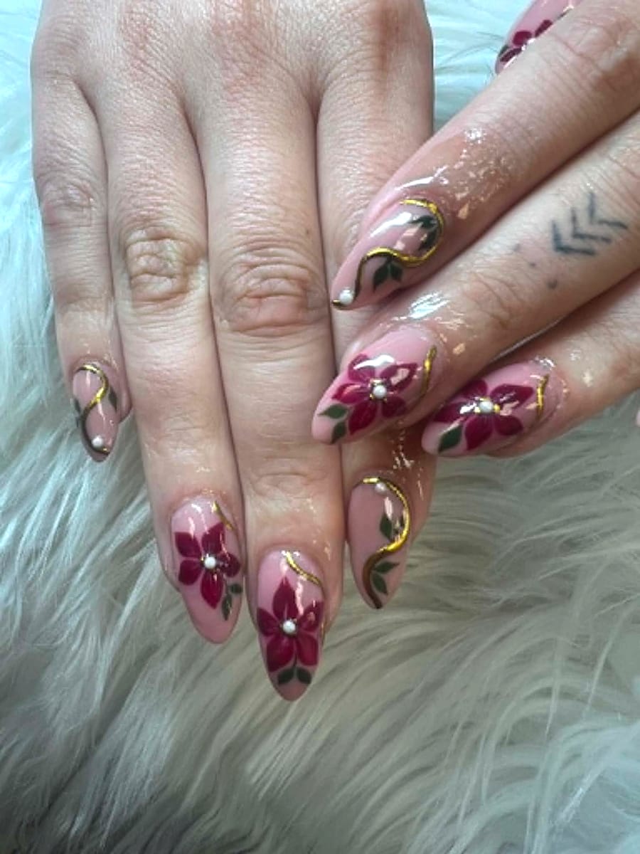 Burgundy floral hand-paint with gold liner and pearl accents on almond nails